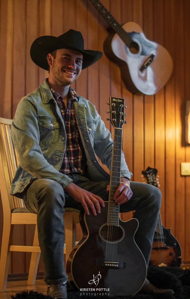 Fabian Gölz hält eine Gitarre in der Hand und lacht in die Kamera